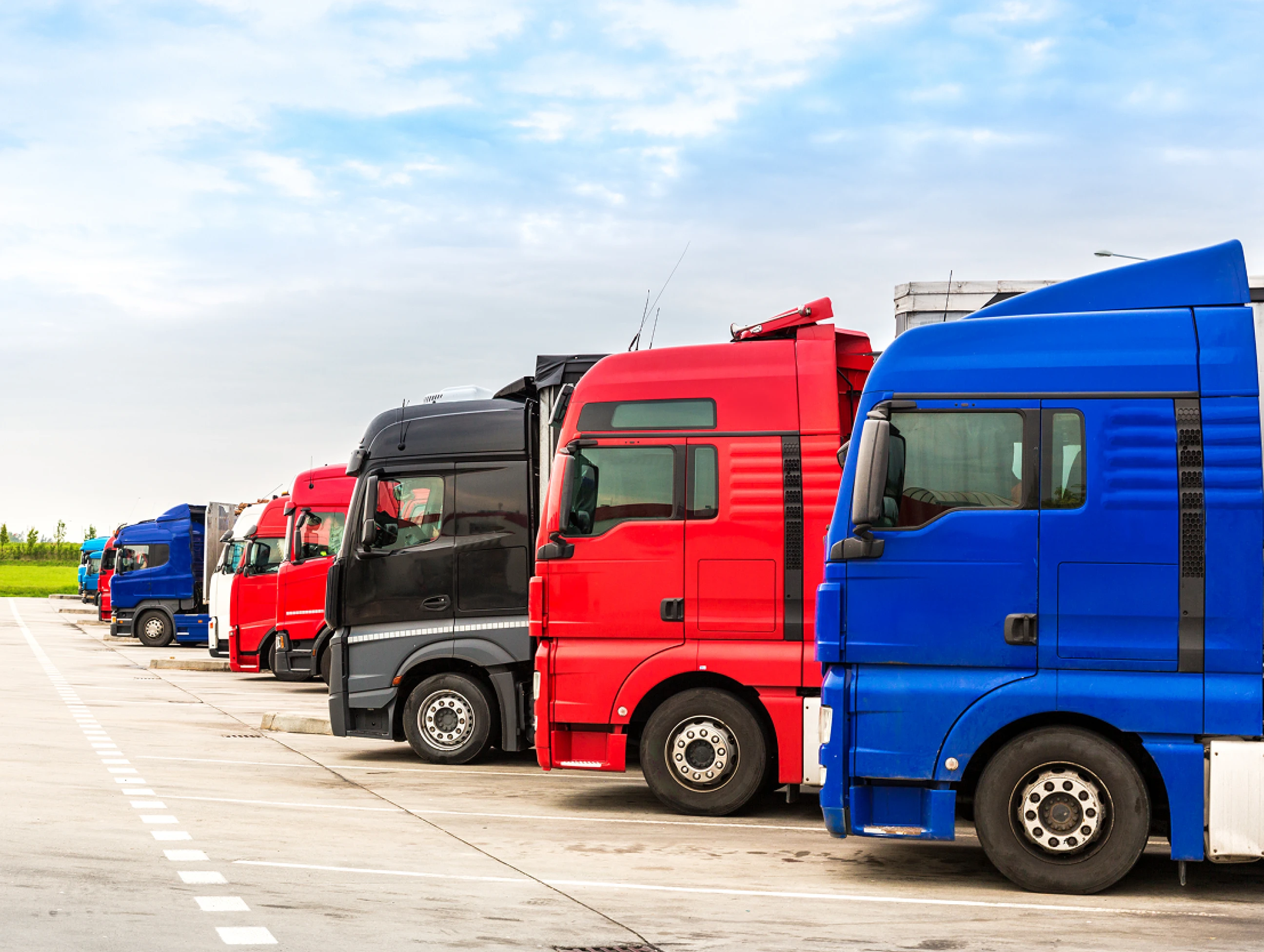 A lineup of parked long-haul trucks in a logistics yard, captured in daylight.